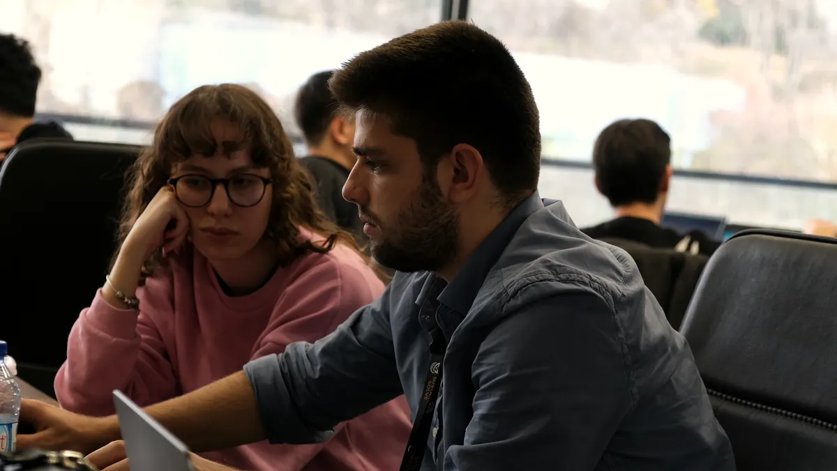İki genç katılımcı dizüstü ekranındaki çözümü birlikte çalışıyor