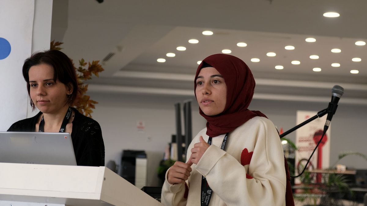 İki genç kadın girişimci kürsüde: biri mikrofonda fikrini anlatıyor, diğeri dizüstünde sunumu yürütüyor