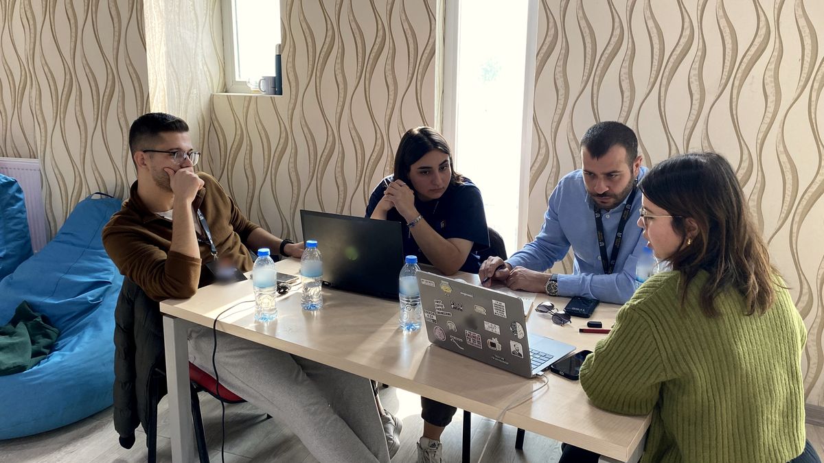 Kurum mühendisi üç genç araştırmacıyla dizüstülerin başında problemi tartışıyor, pencere ışığı
