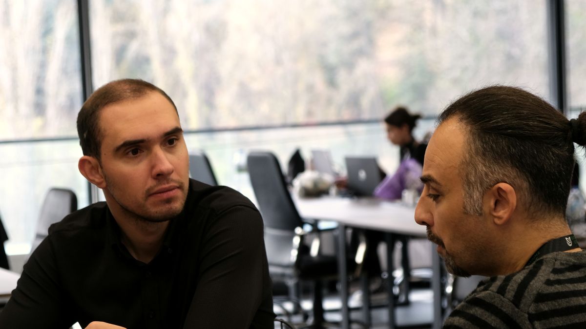 Deneyimli mentor genç katılımcıyla kafe masasında birebir konuşuyor, pencere ışığı